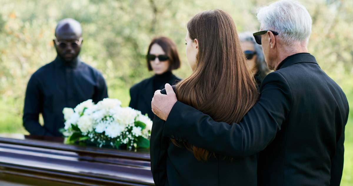 Uitvaart; mensen staan om een kist met bloemen
